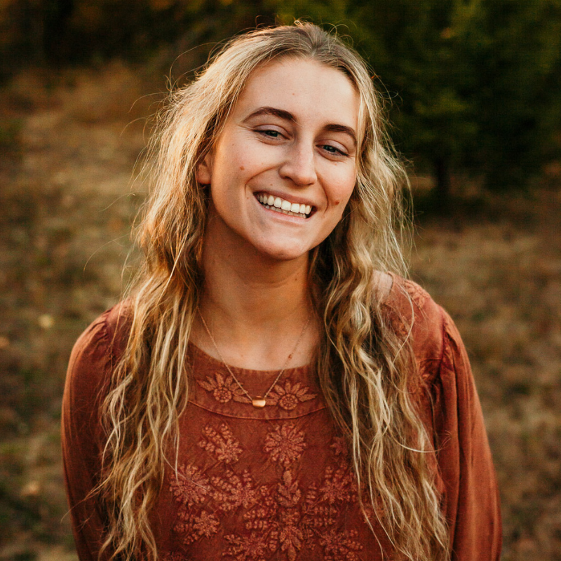 Girl standing in grassy field smiling at camera