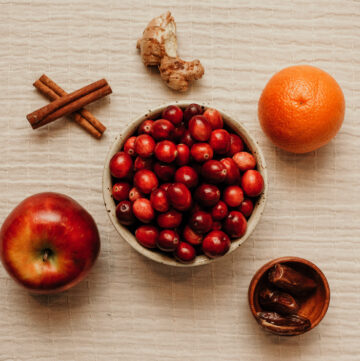 bowl of cranberries surrounded by apple orange and spices